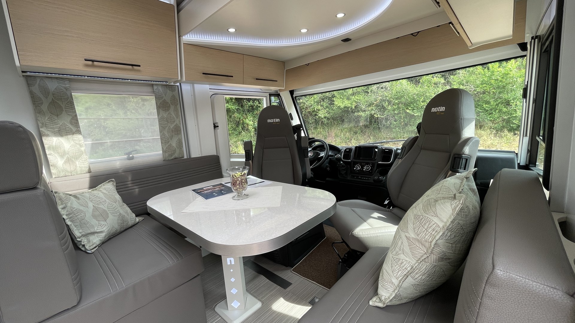 Dinette d'un camping-car intégral Notin avec table centrale, banquettes et sièges cabine pivotés