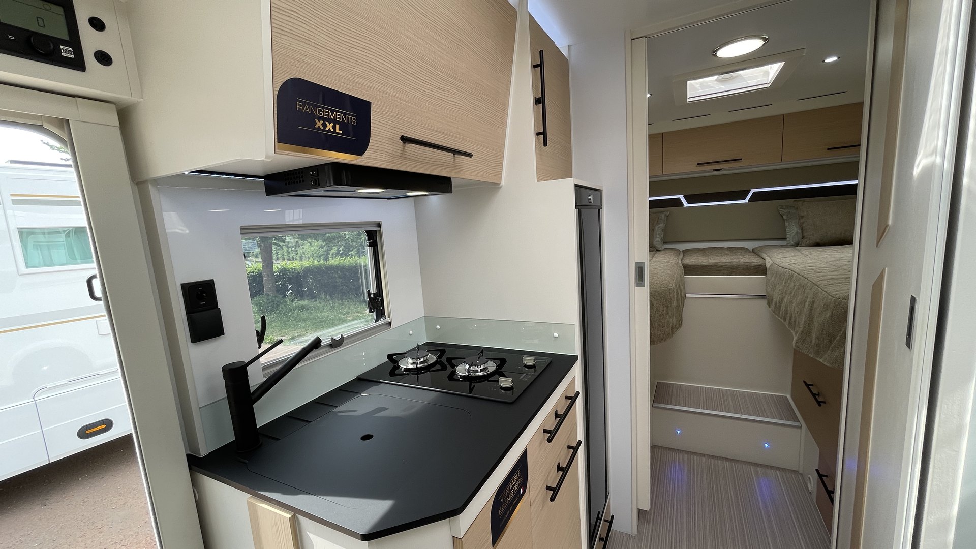 Cuisine d'un camping-car Notin avec placards hauts, réchaud deux feux et accès à la chambre arrière